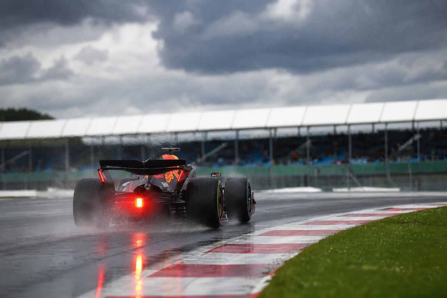 Formula 1 car driving on a wet track under dark, stormy clouds, kicking up water spray with its red rain light glowing.