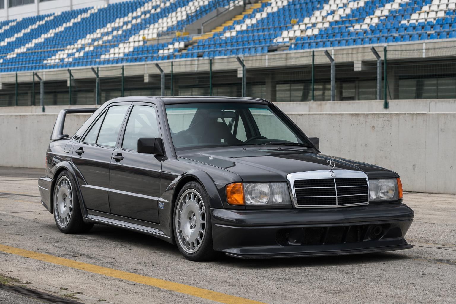 Mercedes 190E Evo II: a engenharia do sedã das pistas Black Mercedes-Benz 190E 2.5-16 Evolution II with a large rear wing and flared arches parked on a racetrack in front of blue and white grandstands.